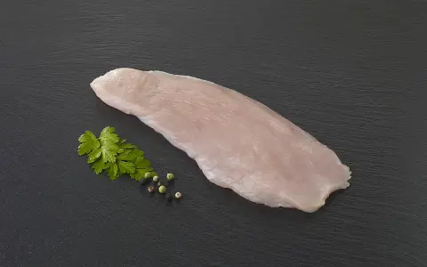 Une escalope de dinde crue, prête à être cuisinée, accompagnée de persil frais et de grains de poivre sur fond sombre.