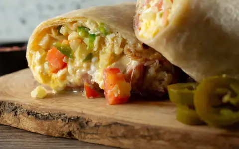 Pyszna tortilla z jajecznicą, pomidorami i papryką, podana na drewnianej desce z plasterkami jalapeno.