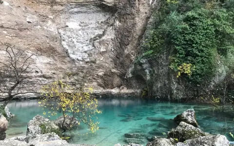 La source de la Sorgue, une eau turquoise limpide émergeant d'une falaise rocheuse, entourée de végétation et d'arbres aux feuilles d'automne.