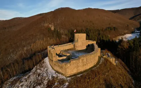 Ruiny zamku w Rytrze, z polską flagą na wieży. Warto sprawdzić zamek w Rytrze cennik przed wizytą.