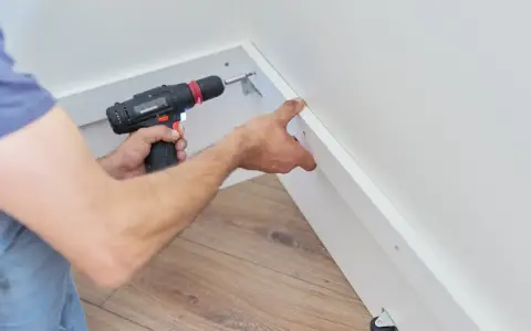 Pose d'une placo sur ossature bois. Un artisan utilise une visseuse pour fixer une plaque de plâtre sur une structure en bois.