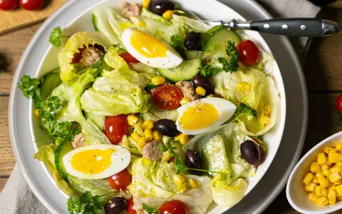 Frischer Salat mit knackigem Eisbergsalat, Tomaten, Gurken, Oliven, Mais und Eiern. Ein herzhafter Thunfischsalat, der Lust auf mehr macht.