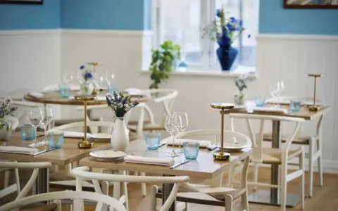 Vackert dukade bord med blåa glas och blommor i vaser, redo för gäster på en av restaurangerna i Skagen.