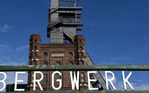 Das alte Bergwerk Prosper Haniel mit seinem markanten Förderturm ragt gegen einen blauen Himmel auf.