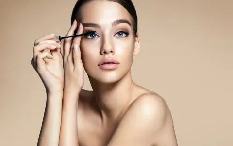 Donna con occhi azzurri applica mascara. Scopri come togliere il mascara waterproof senza irritare la pelle.