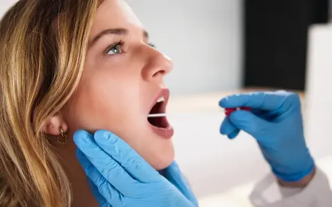 Młoda kobieta z otwartymi ustami, której gardło jest badane patyczkiem do testu strep.