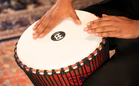 Dłonie grają na djembe, rodzaju bębna o kolorowym korpusie.
