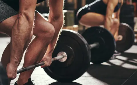 Personer lyfter skivstång i gym. Frågan "hur lång tid tar det att bygga muskler" besvaras med konsekvent träning.