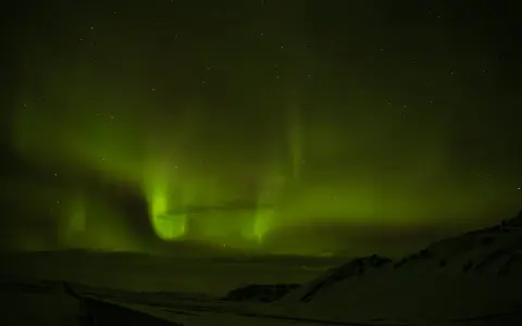 Niesamowita zorza polarna nad Islandią. Zielone smugi tańczą na nocnym niebie, oświetlając ośnieżony krajobraz i drogę.