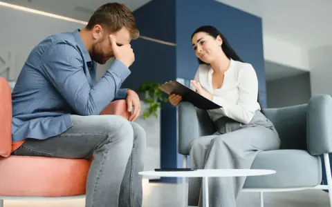 Mężczyzna w stresie podczas sesji, która może być częścią terapii uzależnień online. Terapeutaka notuje.