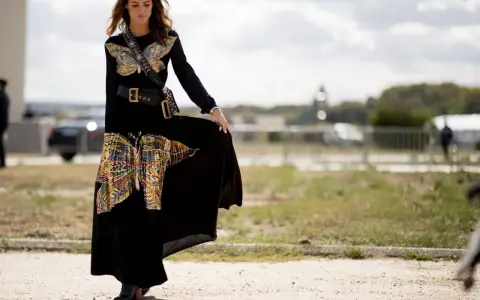Mujer con vestido largo negro con estampado de mariposas, cinturón ancho y botines. Un ejemplo de como llevar un vestido largo informal con estilo.