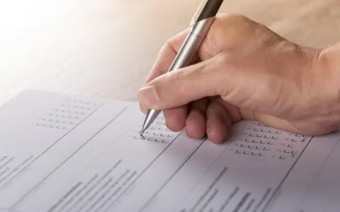 Dłoń z długopisem wypełnia formularz, zaznaczając odpowiedzi. To część procesu tworzenia wykazu majątku.