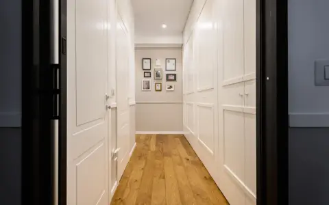 Corridoio con parquet e armadi bianchi. Un'idea per come dividere un corridoio lungo con porte e quadri decorativi.