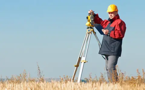 Geodeta w żółtym kasku pracuje z tachimetrem na polu. Zastanawiasz się, ile kosztuje geodeta?