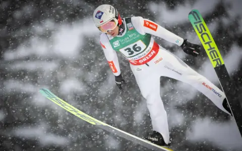 Skoczek narciarski w locie, przygotowuje się do lądowania. Widoczny numer 36. To może być zapowiedź skoki narciarskie 2026.