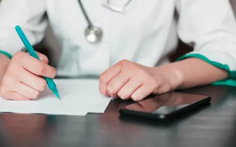 Lekarz pisze zwolnienie, zastanawiając się, na ile lekarz może wystawić L4 jednorazowo. Obok leży telefon.