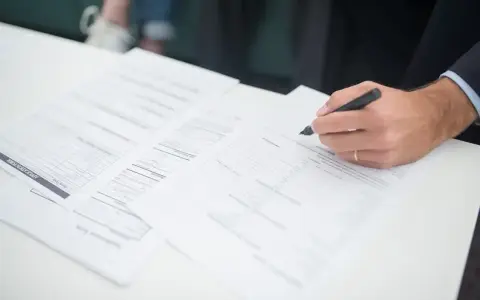 Ręka klienta podpisuje dokumenty ubezpieczeniowe. Agent ubezpieczeniowy czeka na zakończenie formalności.