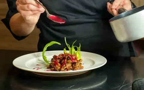 Chef decora un piatto di straccetti di manzo con una salsa rossa brillante, guarnendo con verdure verdi.