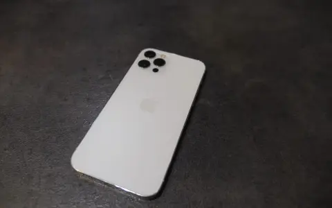 Elegancki, biały iPhone 12 Pro Max z charakterystycznym modułem aparatów na ciemnym tle.