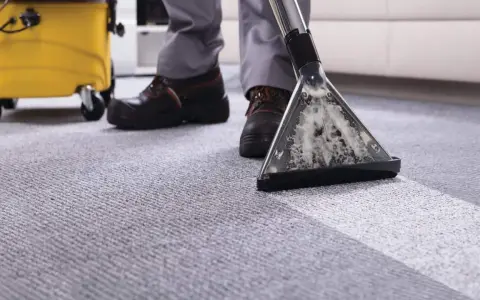 A person demonstrates how to clean a carpet using a professional carpet cleaner, leaving a fresh, clean path.