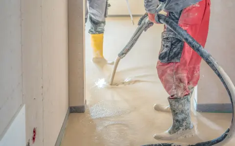 Arbeiter verlegen Estrich mit einer Pumpe. Der flüssige Estrich fließt auf den Boden und wird verteilt.