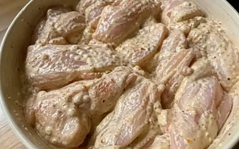 En skål med yoghurtmarinerad kyckling, redo att tillagas. Kycklingbitarna är täckta av en krämig, kryddig marinad.