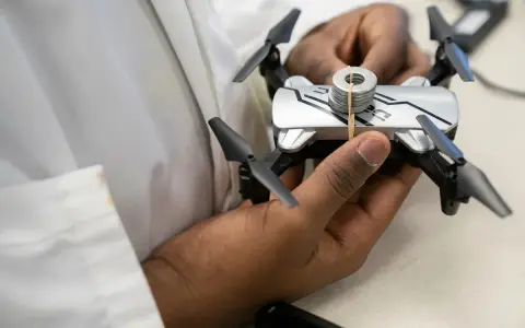 A person holds a small drone with weights attached, perhaps testing its flight capabilities in relation to Oklahoma drone laws.