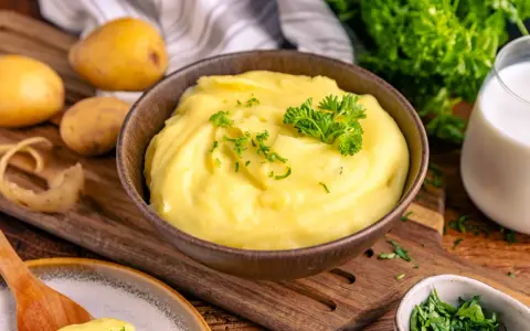 Cremiger Kartoffelbrei, perfekt zubereitet im Thermomix, garniert mit Petersilie. Dazu frische Kartoffeln und ein Glas Milch.