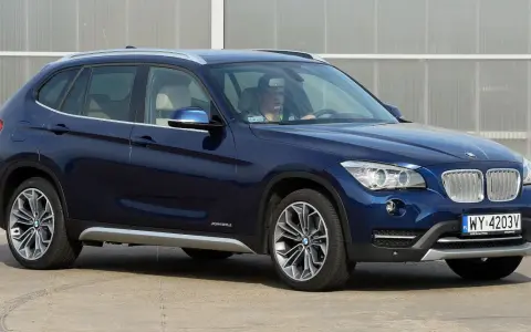 Ciemnoniebieskie BMW X1 E84 z kierowcą za kierownicą, zaparkowane na zewnątrz.