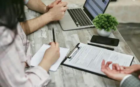 Réunion pour une contre-expertise assurance : un contrat est sur la table, un ordinateur portable ouvert, et des mains discutent des détails.