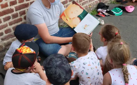 Un animateur lit un livre illustré à des enfants assis en cercle. L'image évoque un moment de partage et d'apprentissage, comme un diplôme animation.