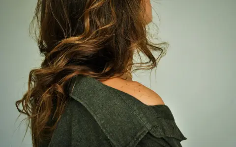 Spalle scoperte e capelli castani mossi, un dettaglio di donne con pochi capelli che incornicia il volto.