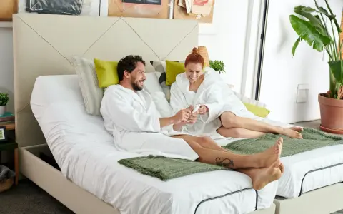 Pareja en bata blanca sobre cama articulada, aprendiendo como vestir una cama articulada para mayor comodidad.