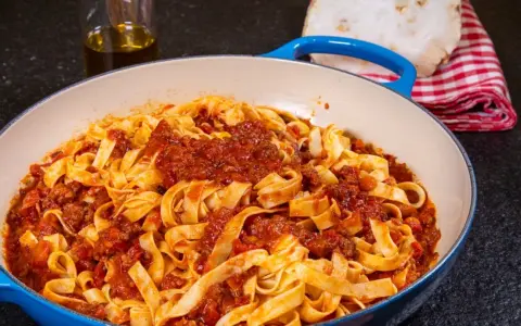 Herzhafte Tagliatelle mit einer reichhaltigen alla bolognese Sauce in einer blauen Pfanne, bereit zum Servieren.