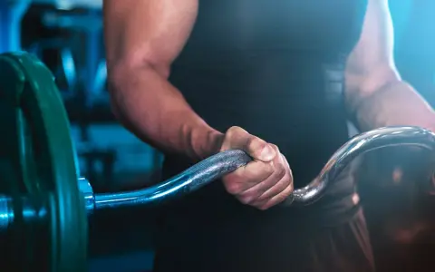 Muskulös arm som greppar skivstång i ett superset gym.