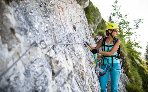 Kobieta w kasku i sprzęcie wspinaczkowym pokonuje via ferrata polska. Wspinaczka po skalnej ścianie z liną asekuracyjną.
