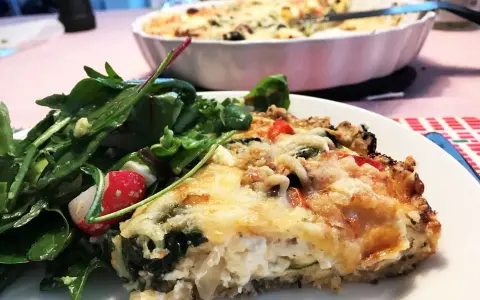 En bit krämig vegetarisk paj med ost och grönsaker, serverad med en fräsch sallad.