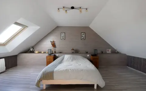 Chambre sous comble avec lit douillet, velux et décoration murale en bois.