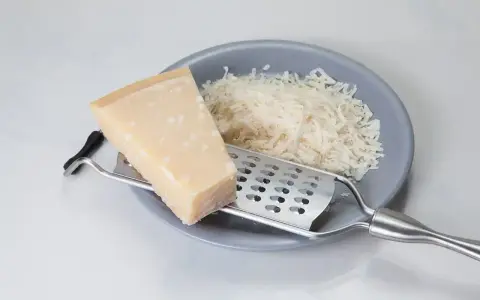 Kawałek parmezanu i starty ser na talerzu. Zastanawiasz się, czy parmezan można mrozić? Tak, można go mrozić, zachowuje wtedy smak.