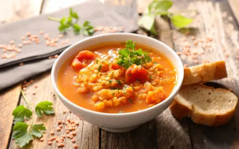 Eine dampfende Schüssel mit herzhafter rote linsensuppe, garniert mit Petersilie, daneben knuspriges Brot auf rustikalem Holztisch.