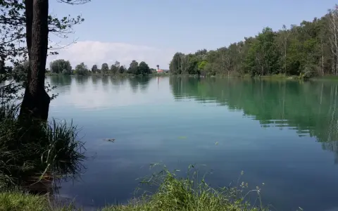 Idyllischer ersinger badesee mit grünen Ufern und einem Kirchturm in der Ferne.