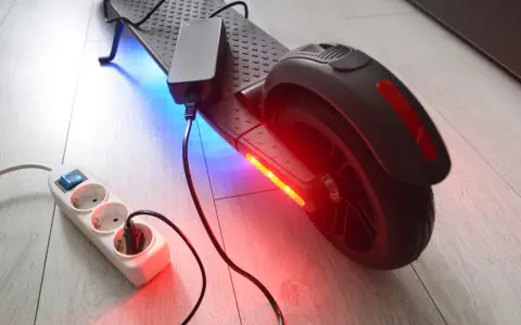 Un chargeur pour trottinette électrique est branché sur une multiprise. La trottinette est éclairée par des LED bleues et rouges.