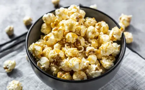 Un bol rempli de pop corn sucré, avec quelques grains éparpillés autour. Un délice croustillant pour une soirée cinéma.