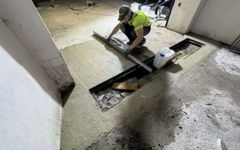 Pracownik wykonuje naprawę posadzki betonowej, wyrównując świeżą masę za pomocą łaty.