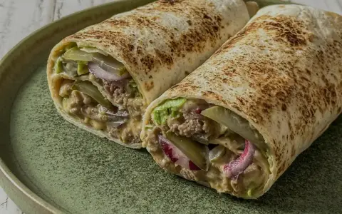 Zwei saftige Big Mac Wraps mit Hackfleisch, Salat, Gurken und Zwiebeln auf einem grünen Teller.