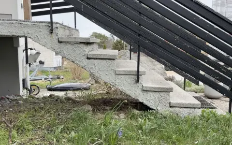 Grå betongtrappa med svarta räcken. En trailer och takbox syns i bakgrunden. Undrar du över gjuta trappa kostnad?
