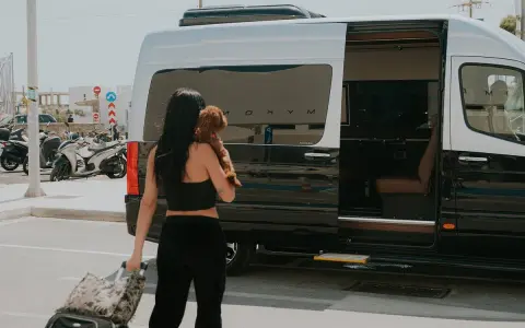 Frau mit Hund und Koffer steigt in Mykonos in einen Van. Ein typischer Anblick auf Reisen über Griechenland.