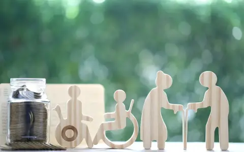 Skarbonka z monetami i drewniane figurki symbolizujące wsparcie dla osób starszych i niepełnosprawnych. Świadczenie wspierające punkty to szansa na lepsze jutro.