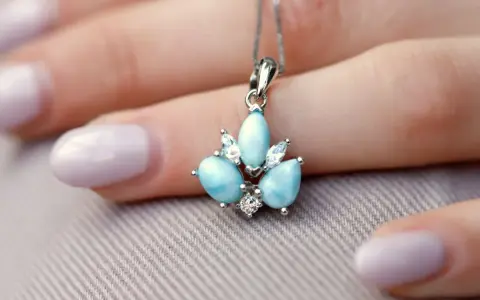 Un ciondolo con una splendida larimar pietra, incastonata con zirconi, adagiato su una mano con unghie lilla.