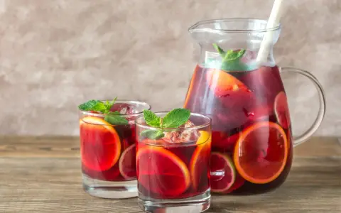 Dwa szklanki i dzbanek pełne orzeźwiającej Sangrii czerwonej z plasterkami pomarańczy i limonki, ozdobione miętą. Idealny wybór na lato!